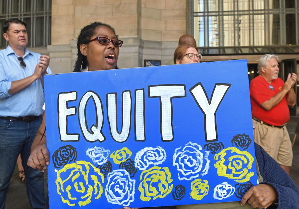 Woman holds up sign that says EQUITY
